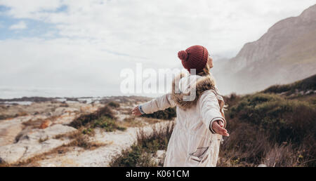 Außenaufnahme der jungen Frau auf einem Winter Tag am Strand. Freudige weibliche an einem Wintertag mit ihren ausgestreckten Armen entlang der Küste. Stockfoto