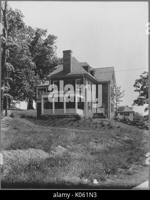 Portraitfotos aus einem 3-stöckigen Haus auf einer geneigten Wiese, mit einem weißen Veranda, ein Schornstein, und von Bäumen mit Blättern umgeben, Roland Park/Boston, USA, 1910. Dieses Bild wird von einer Reihe dokumentieren den Bau und den Verkauf von Wohnungen in der Roland Park/Guilford Nachbarschaft von Baltimore, einer Straßenbahn Vorort und eines der ersten geplanten Gemeinschaften in den Vereinigten Staaten. Stockfoto