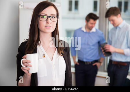 Geschäftsfrau Holding Coffee Mug, während Kollegen diskutieren Stockfoto