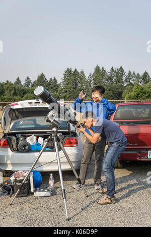 Linn County Oregon State USA, 21. August 2017: jungen asiatischen Hochschulabsolventen aus Kalifornien eingerichtet Teleskop für die Wiedergabe von eclipse vom Parkplatz mit Blick auf die Landstraße in der Nähe der Stadt Sweet Home. Beide arbeiten für ein Unternehmen zu entwerfen & wissenschaftliche Spielzeug für Kinder Credit: Dorothy Alexander/Alamy leben Nachrichten Stockfoto