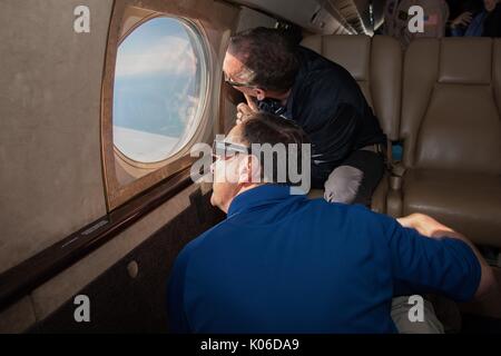 Die NASA-Administrator Robert Lightfoot, Vordergrund, und NASA-Administrator Associate für die Science Mission Directorate Thomas Zurbuchen um die Sonnenfinsternis von an Bord eines NASA Armstrong Flug Forschungsstelle Gulfstream III August 21, 2017 Flying 35.000 Fuß über der Küste von Oregon. Die totale Sonnenfinsternis über einem schmalen Teil des angrenzenden Vereinigten Staaten von Oregon nach South Carolina und eine partielle Sonnenfinsternis war über den gesamten nordamerikanischen Kontinent sichtbar zusammen mit Teilen von Südamerika, Afrika und Europa. Stockfoto