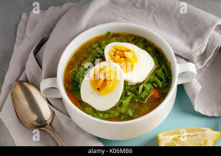 Grüne Gemüse Suppe mit Ei. Teller mit Essen auf dem Tisch mit Löffel und Zitrone Stockfoto