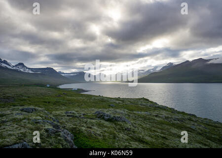 Island - Sonne bricht durch die Wolken am Fjord mit Bergen und grünen Moos bedeckte Landschaft Stockfoto