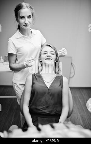 Wunderschöne junge Frau Zahnarzt Zähne Ihrer Patienten zu prüfen, die in einer speziell ausgestatteten Gehäuse. Schwarz-weiß Foto. Stockfoto