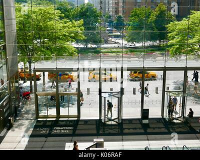 Yellow Cabs ausgerichtet werden, um an den bordstein als durch das Atrium Glas der Geschäfte am Columbus Circle New York, NY, USA gesehen. Stockfoto