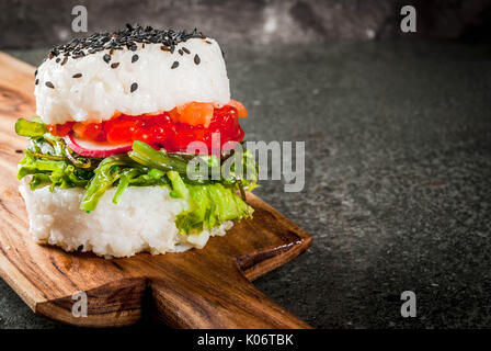 Trend hybrid Essen. Japanische asiatische Küche. Sushi-Burger, Sandwich mit Lachs, hayashi Wakame, daikon, Ingwer, roter Kaviar. Schwarz Tisch aus Stein, mit Soja Stockfoto