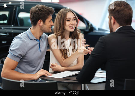 Selbstbewussten jungen Verkäufer erklären, alle neuen Auto kennzeichnet den jungen attraktiven Besitzer Stockfoto