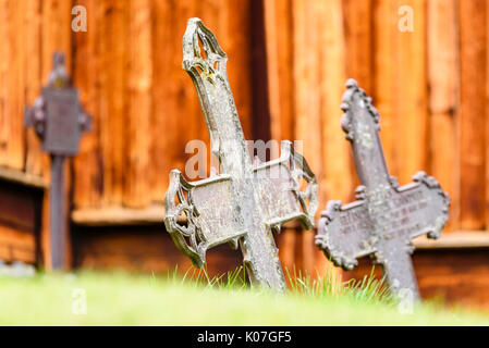 Alte Metall Kreuze mit Kirche aus Holz Wand im Hintergrund. Niedrigen Winkel mit grünen Gras im Vordergrund. Stockfoto