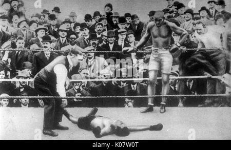 Jack Johnson (1878-1946), der den Spitznamen die Galveston Giant, Afro World Heavyweight Champion Boxer, 1908-1915, stehend an den Seilen in einem Boxkampf mit einem unbekannten Gegner, der offensichtlich heraus geklopft worden. Um 1910 Stockfoto