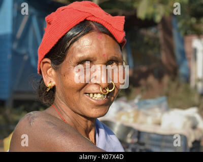 Ältere indische Adivasi-Frau mit zwei goldenen Nasenringen und markanten Stammesohrringen lächelt für die Kamera. Stockfoto