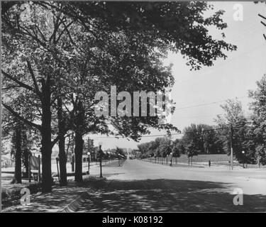 Foto von einer Straße in Baltimore, mit Kugel - wie Straßenlaternen, die Straße ohne Autos, und nur ein paar Fußgänger, eine glatte asphaltierte Straße mit vielen schattigen Bäumen auf den Bürgersteigen, United States, 1920. Dieses Bild wird von einer Reihe dokumentieren den Bau und den Verkauf von Wohnungen in der Roland Park/Guilford Nachbarschaft von Baltimore, einer Straßenbahn Vorort und eines der ersten geplanten Gemeinschaften in den Vereinigten Staaten. Stockfoto