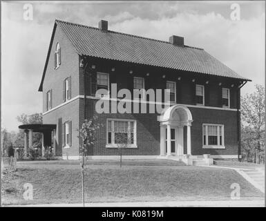 Foto von der Außenseite des Ziegels in Baltimore, Maryland mit Windows mit und ohne Fensterläden, Schornsteine, und zwei kleine Treppen, die zu einem überdachten Eingangsbereich, in einem spärlich Landschaften Rasen in einer Wohnstraße mit einem Bürgersteig in Baltimore, Maryland, 1910. Dieses Bild wird von einer Reihe dokumentieren den Bau und den Verkauf von Wohnungen in der Roland Park/Guilford Nachbarschaft von Baltimore, einer Straßenbahn Vorort und eines der ersten geplanten Gemeinschaften in den Vereinigten Staaten. Stockfoto