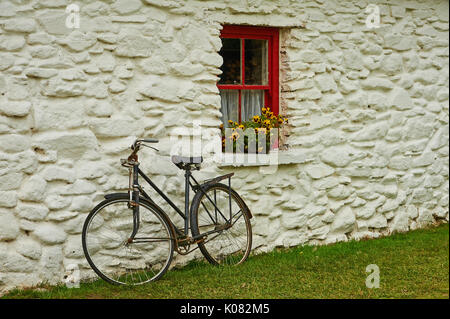 Ein altes Fahrrad gegen ein Kalk schiefen gewaschen Gebäude aus Stein mit einem rot lackierten Fenster und gelbe Blumen Stockfoto