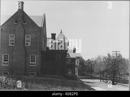 Seitenansicht von Backstein Haus in einer ruhigen Straße, Haus hat 4 große Fenster seitlich, Kamin und Veranda, Veranda mit Blick auf Bäume, freien Platz mit Vegetation an der Seite des Hauses, Baltimore, Maryland, 1910. Dieses Bild wird von einer Reihe dokumentieren den Bau und den Verkauf von Wohnungen in der Roland Park/Guilford Nachbarschaft von Baltimore, einer Straßenbahn Vorort und eines der ersten geplanten Gemeinschaften in den Vereinigten Staaten. Stockfoto