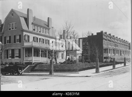 Wohn- Straße Ecke in Baltimore, Maryland, mit Bäumen gesäumten Gehsteig, ein Auto außerhalb der ein großes Haus mit einem oberen und unteren Veranda geparkt, mehrere Schornsteine, und sowohl Standard- als auch Fenster mit Fensterläden, neben einer Reihe von Reihenhäusern, jedes mit einer vorderen Schornstein, Gauben und eine Treppe, die zu einer Veranda, Baltimore, Maryland, 1910. Dieses Bild wird von einer Reihe dokumentieren den Bau und den Verkauf von Wohnungen in der Roland Park/Guilford Nachbarschaft von Baltimore, einer Straßenbahn Vorort und eines der ersten geplanten Gemeinschaften in den Vereinigten Staaten. Stockfoto