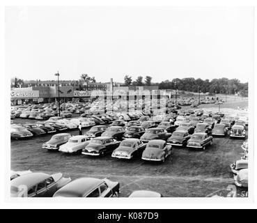 Parkplatz von Northwood Einkaufszentrum mit Hunderten von Autos, speichert im Hintergrund einschließlich Acme Märkte und liest, Bäume und Häuser im Hintergrund, Parkplatz hat viele Lichter der Stadt, Baltimore, Maryland, 1930. Stockfoto