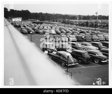 Parkplatz von Northwood Einkaufszentrum mit Hunderten von Autos, Zeichen im Hintergrund, die lautet: "Sie in der Marine sind Jetzt', Bäume, Häuser und Straßenbeleuchtung im Hintergrund, Baltimore, Maryland, 1951. Stockfoto