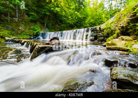 Schöne kleine Wasserfall auf der schönen Bach im Wald in der Tschechischen. Lange Belichtungszeit, milchiges Wasser Effekt, Bäume und grüne Gras um, Felsen und Steine Stockfoto