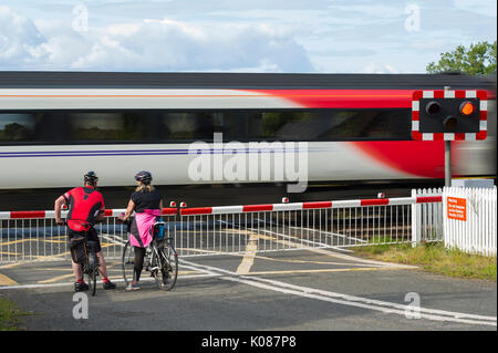 Zwei Radfahrer warten, bis eine Jungfrau Zug an einem Bahnübergang auf der East Coast Main Line in der Nähe Aberlady, East Lothian Stockfoto