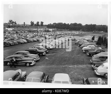 Blick auf einem Parkplatz, im Bau, im Hintergrund ist ein Teil der Northwood Shopping Center und hinter dem Zentrum sind row Wohnungen links und Bäume auf der rechten Seite, ist eine Person auf dem Weg zu ihrem Auto im Vordergrund, Baltimore, Maryland, 1951. Stockfoto