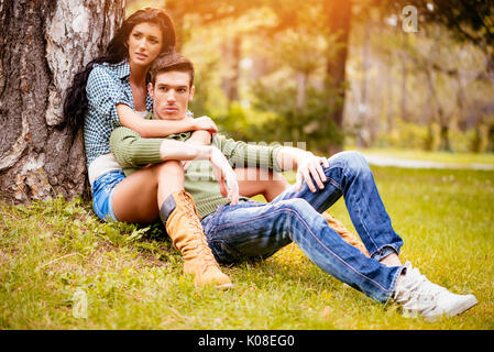 Schöne Paar schöne sitzen auf der Wiese neben dem Baum und genießen im sonnigen Park in herbstlichen Farben. Stockfoto