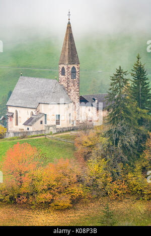 Kirche durch die herbstlichen Bäume und Nebel umgeben. Santa Maddalena, Funes, Bozen, Trentino Alto Adige, Südtirol, Italien, Europa. Stockfoto