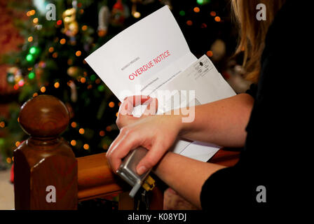 Eine Frau hält eine Mahnung, Weihnachtsbaum im Hintergrund. Stockfoto