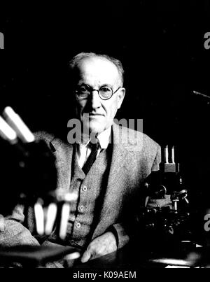 Halbe Länge Foto von Dr. Samuel Mast, Biologie Mitglied der Fakultät an der Johns Hopkins Universität, hinter einem Schreibtisch aus Holz, trug einen dunklen Anzug und drei Stück runder Brille, ein Mikroskop und andere Instrumente auf dem Tisch vor ihm, mit einem ernsten Gesichtsausdruck. 1937. Stockfoto
