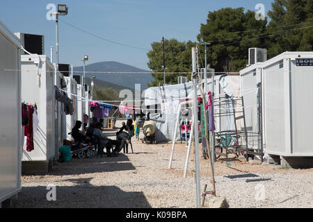 Männer im Schatten sitzen zwischen den Reihen von vorgefertigten Unterkünfte in Ritsona Flüchtlingslager, Griechenland. Stockfoto