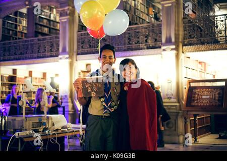 Zwei Studenten stellen mit ihren Armen um jeden anderen, der Junge ist, wie die Hauptfigur in dem Film 'Nach oben' und das Mädchen trägt einen schwarzen Outfit und rotem Mantel, 2015 bekleidet. Stockfoto