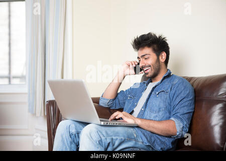 Asiatischer Mann mit einem Laptop und am Telefon sprechen zu Hause in der Lounge. Stockfoto