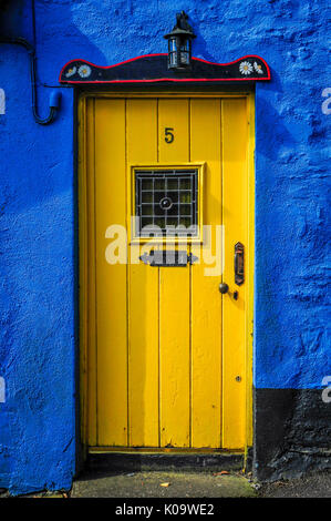 Eine helle gelbe Tür hebt sich der blaue Fassade ein kleines Häuschen Stockfoto