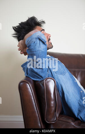 Seitenansicht eines müde oder unglücklich asiatischer Mann sitzt auf einem Sofa seinen Kopf halten. Stockfoto