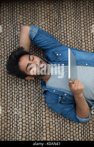 Inder auf dem Boden liegend zu Hause seinen Tablet-PC lesen. Oben betrachten. Stockfoto