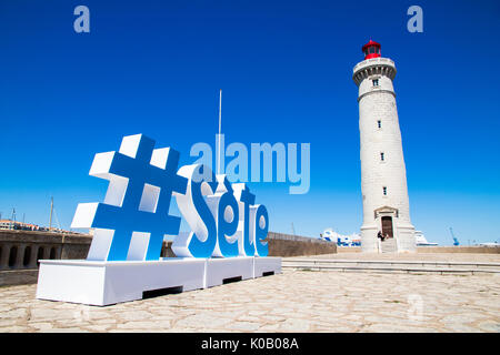 Die Phare du Mole Saint-Louis, einem weißen und roten Leuchtturm in Sete, Südfrankreich, mit einem Schild mit einem Hashtag und den Namen der Stadt in der foregro Stockfoto