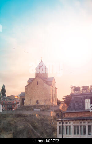 Ein Blick über die Dächer von alten Häusern, Mtkvari (Kura) Fluss und Metekhi Kirche im Zentrum von Tiflis, Georgien, und ein Sonnenaufgang am frühen Morgen. Stockfoto