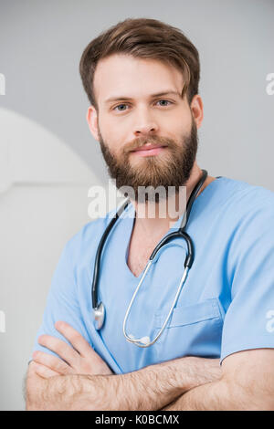 Männlicher Arzt stehende Arme im Untersuchungsraum gekreuzt Stockfoto