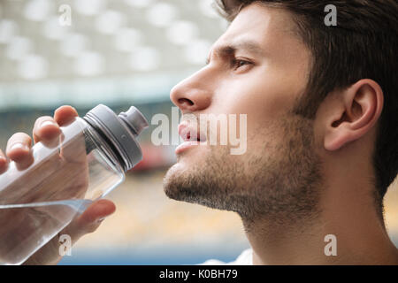 Close up Profil Portrait von ein stattlicher Mann von Trinkwasser aus einer Flasche im Stadion Stockfoto