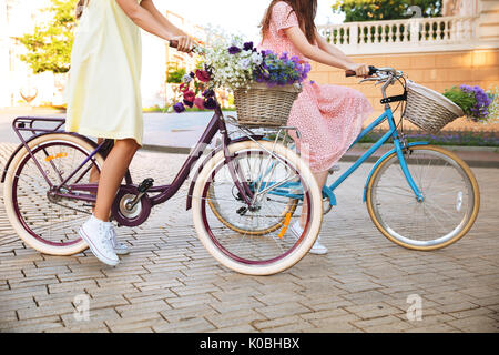 7/8 Seitenansicht Bild von zwei jungen Frauen in Kleidern, retro Fahrrad auf einer Straße der Stadt Stockfoto