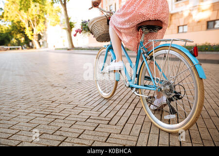7/8 Bild einer jungen Frau in Kleid Reiten Fahrrad im Freien Stockfoto