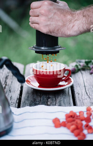 Leckere, frische Morgen filter Kaffee tropft in die keramische red Cup auf dem alten rustikalen Tisch Hintergrund Stockfoto