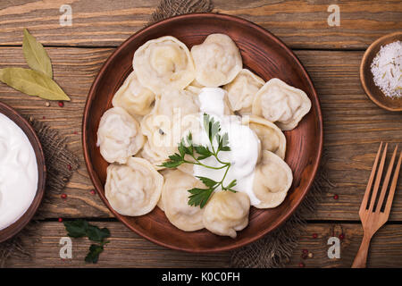 Hausgemachte Fleisch Knödel - russische Pelmeni mit saurer Sahne und Petersilie Nahaufnahme, Ansicht von oben Stockfoto