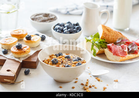 Müsli mit Joghurt, Sandwiches mit Fleisch und Avocado und mini Käsekuchen mit Heidelbeeren zum Frühstück. Stockfoto