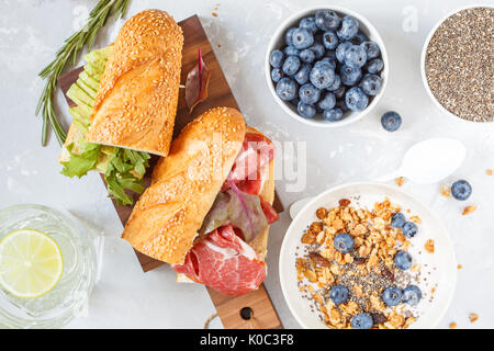 Müsli mit Joghurt, Sandwiches mit Fleisch und Avocado und mini Käsekuchen mit Heidelbeeren zum Frühstück. Stockfoto