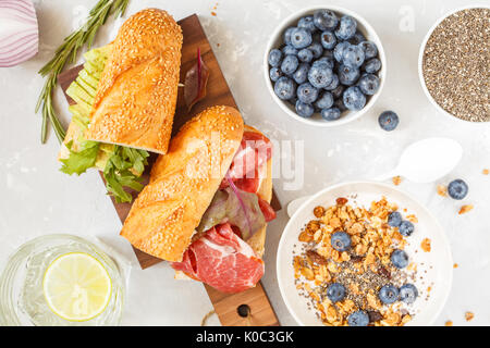 Müsli mit Joghurt, Sandwiches mit Fleisch und Avocado und mini Käsekuchen mit Heidelbeeren zum Frühstück. Stockfoto