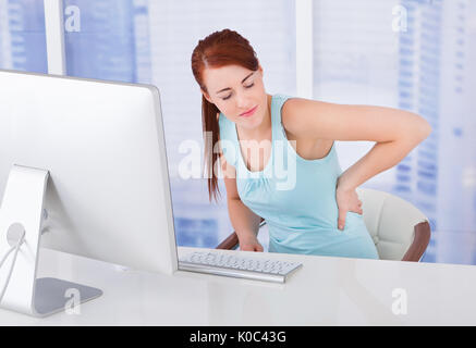 Junge Geschäftsfrau leiden unter Rückenschmerzen bei Computer-Schreibtisch im Büro Stockfoto