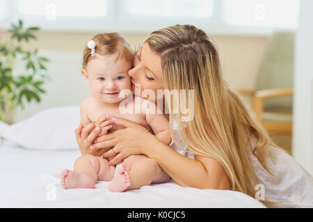 Mutter umarmt ein Baby Kind auf einem Bett in einem Zimmer im Innenbereich. Stockfoto