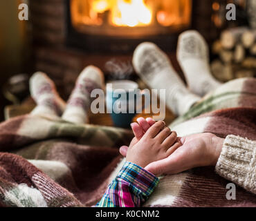 Wärmend und entspannend in der Nähe von Kamin. Mutter und Tochter, die Hand in Hand vor Feuer. Stockfoto