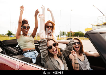 Bild der glücklichen emotionale vier junge Frauen, die Freunde sitzen im Auto im Freien. Stockfoto