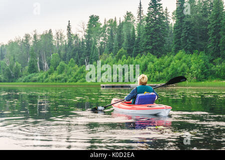 Frau in einem Kajak paddeln entlang des Seeufers, Alberta, Kanada Stockfoto